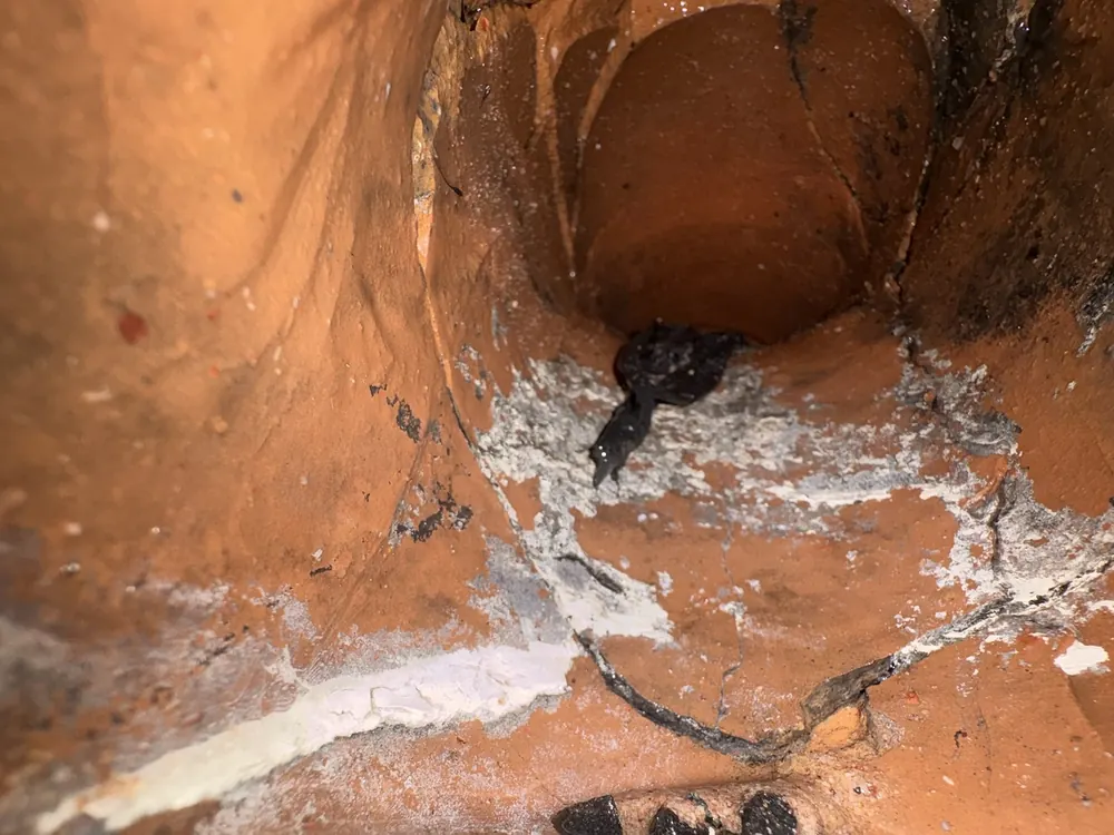 Inside an old clay drain pipe showing cracks and damage at a joint.